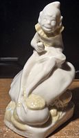 Front view of the Belleek porcelain leprechaun figurine sitting on a shaped base with yellow highlights.