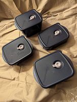 Four blue plastic Tupperware containers with vented lids arranged to show size variation and vent valve detail.