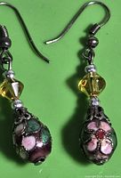 Close-up front view of one cloisonné earring showing floral pattern on bead, yellow faceted bead, and metal hook.