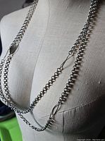 Long multi-strand silver-tone necklace displayed on a dress form, showing chain style and leaf embellishments.