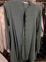 Green long buttoned shirt hanging on a rack, front view showing button details and fabric texture.