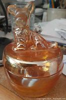 Single image of Jeanette Luster carnival glass covered dish with terrier motif on lid, amber gold glossy finish.