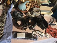 Image showing men's dress belts, neckties, and bowties laid out on a surface. Varied colors and styles visible, including new packaged tie.