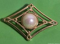 Close-up of the front showing the elongated diamond shape brooch with a large round faux pearl in the center, showcasing twisted and smooth gold-tone metal details.