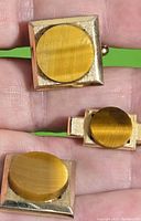 Close-up showing tiger's eye cufflinks and tie clip held in hand, displaying size and detail of stones and metalwork.