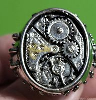 Close-up front view of the steampunk style men's ring showing detailed silver and brass-tone mechanical gear motifs on oval face.
