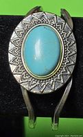 Silver bracelet with a large oval turquoise stone in the center, showing engraved heart patterns on the silver surrounding the stone.