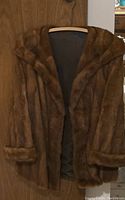 Front view of brown fur coat hanging on wooden door, showing wide collar and cuffs.