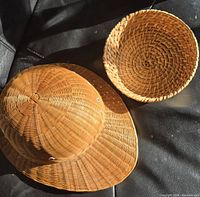 Photo showing a woven wicker hat with wide brim and small round wicker basket together on black surface.