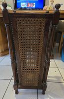 Side view showing cane work panel framed by dark wood with turned posts and finials.