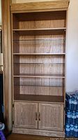 Full front view of the bookcase showing all shelves and cupboard doors, highlighting the laminate wood finish and overall wear.