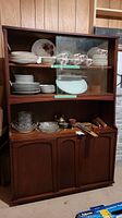 Front view of retro wood china cabinet filled with dishware and glassware inside sliding glass doors and wooden doors below.
