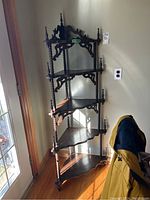 Full view of dark wooden corner stand with five tiered shelves in a corner by a window, showing turned spindles and finials.