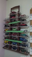 Full view of plastic display shelf unit mounted on wall with multiple model cars and 'History of Ford' sign attached on top