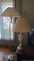 Gold tone floor lamp and beige table lamp side by side showing full lamp bodies and shades