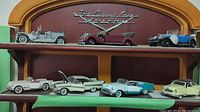 Full view of seven Franklin Mint diecast car models displayed on two wooden shelves, showing various colors and styles representing classic cars from early to mid 20th century.