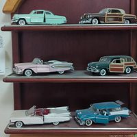 Six Franklin Mint diecast model cars on wooden shelves showing variation in color, style, and detailed features including opening doors.