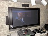 Front view of LG 41-inch flat panel TV mounted on wall with two remotes and assorted electronics below.