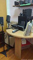Photo showing five black Logitech speakers, amplifier, and two webcams on a wooden table and stands.