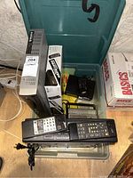 Photo showing Motorola Shawdirect receiver, stacked remotes, and assorted electronics on floor near plastic bins and boxes