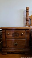 Front view of the wooden nightstand showing two drawers with distinct pulls and carved shell design on upper drawer.