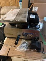 Oster pizza oven with thermostat control knob, Hamilton Beach indoor electric griller, electric rotisserie parts including skewer and motor unit, and Grillpro universal adjustable rock grate partially visible on top.