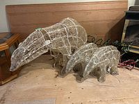Full view of three white wire frame polar bears: one large mama bear and two smaller cubs. Lighted decoration setup indoors on wooden floor.