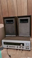 Pair of vintage wooden speakers with grey fabric grille and silver front panel stereo receiver below them on a wooden surface.