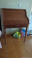 Front view of the wood roll top desk showing curved slatted roll top and carved legs.