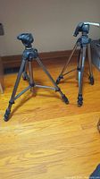 Both tripods standing on hardwood floor, showing overall condition and design.