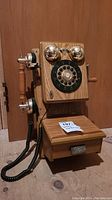 Front view of vintage wood wall phone highlighting rotary dial, gold-tone bells, and lower wooden compartment.