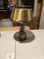 Front view of antique lamp showing its heavy metal shade, square base, and wrapped cord.