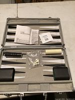 Full view of backgammon board inside open metal case with game instructions, black and white checkers, dice, dice cups and doubling cube.
