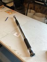 Full view of chrome adjustable doorway chin up bar resting on a white folding table, showing black foam grips and chrome ends.