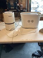 Levoit dehumidifier and Honeywell air cleaner side by side on table with cords visible