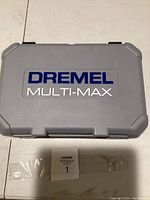 Closed grey plastic case with Dremel Multi-Max logo on lid, placed on white surface, showing case condition.