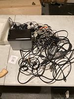 Top-down view of tangled cables and a black electronic box on a white surface.