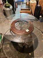 Top view of round beveled glass table with visible ornate wooden frame and metal base decorative element.
