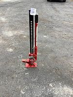 Front and left side view of the red mechanical jack positioned outdoors on asphalt.