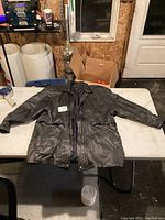 Full view of black leather jacket laid flat showing front with zipper and arm details.