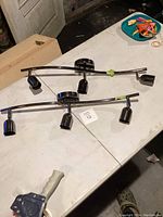 Two larger curved track light fixtures with three black adjustable lamp holders each on a silver curved bar.