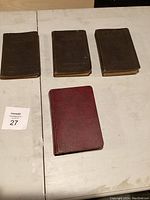 Four old books on a table; three with dark covers and one red.