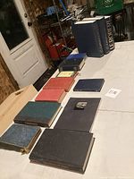 Photo of 11 assorted old books laid out on a table showing various colors, sizes, and conditions.