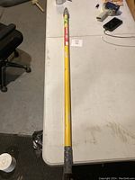 Full length view of the yellow paint pole lying on a white table showing the worn condition and attachments.