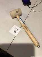 Rubber mallet showing wood handle and white rubber head on a white table with lot number 73 visible.