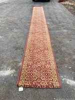 Full length view of the long carpet runner laid out on a rough pavement to show entire length and pattern distribution.