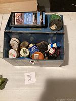 Overview of shoe polish kit contents from above showing multiple tins, brush, and cleaner box inside blue metal box.