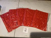 Five new packs of bright red silicone chocolate molds shaped as alphabet letters A to Z, still in their original plastic packaging, laid out flat on a white surface.