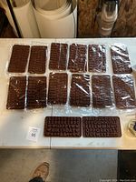 Full view of 12 brown silicone chocolate molds sealed in plastic wrap on a white table, including alphabet and numeric molds