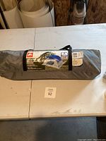 Full view of the tent in carry bag lying on a table, gray carry bag with handle strap.